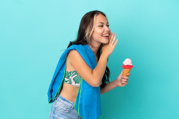 Chica caucásica adolescente sosteniendo helado y toalla aislada de fondo azul gritando con la boca abierta a un lado