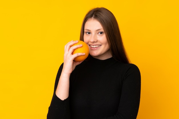 Chica caucásica adolescente sosteniendo una naranja sobre amarillo aislado