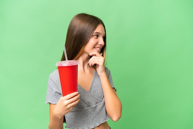 Chica caucásica adolescente sosteniendo un refresco sobre un fondo aislado pensando en una idea y mirando de lado