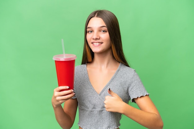 Chica caucásica adolescente sosteniendo un refresco sobre un fondo aislado con los pulgares hacia arriba porque algo bueno ha sucedido