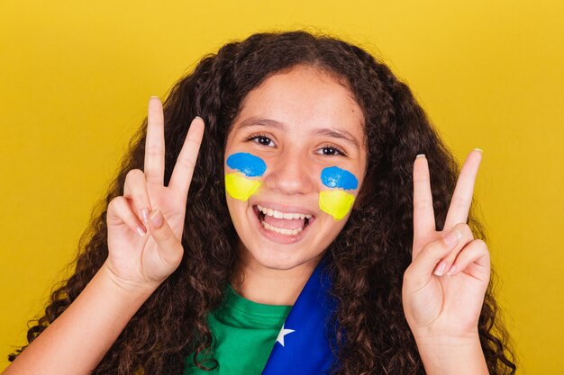 Chica caucásica brasileña hincha de fútbol foto de primer plano expresión de paz y amor dedos levantados pose feliz para la foto Olimpiadas de la Copa Mundial