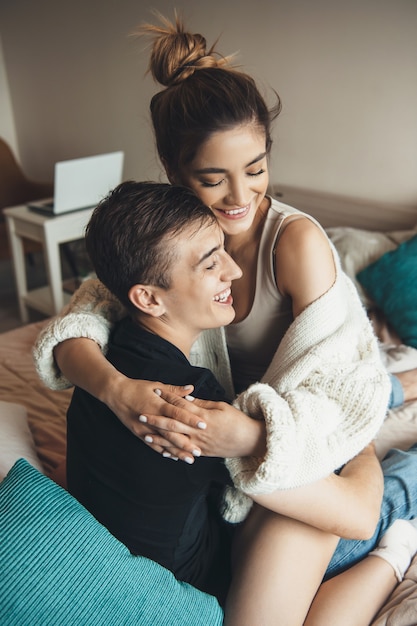 Chica caucásica con cabello castaño abrazando a su amante en la cama y sonrisa