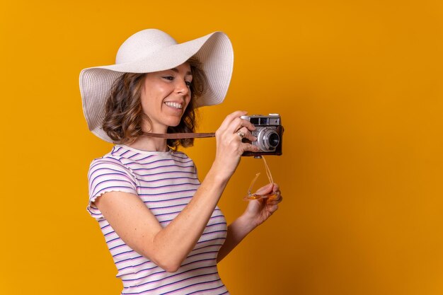 Chica caucásica en concepto turístico con gafas de sol y cámara fotográfica en un fondo amarillo