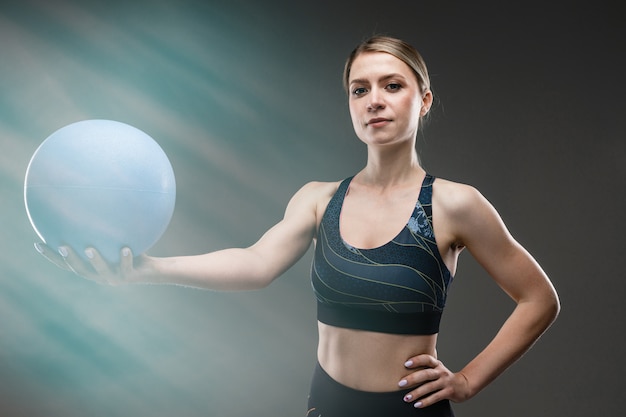 Chica caucásica deporte con figura delgada hacer ejercicios con pelota azul aislado en la pared negra