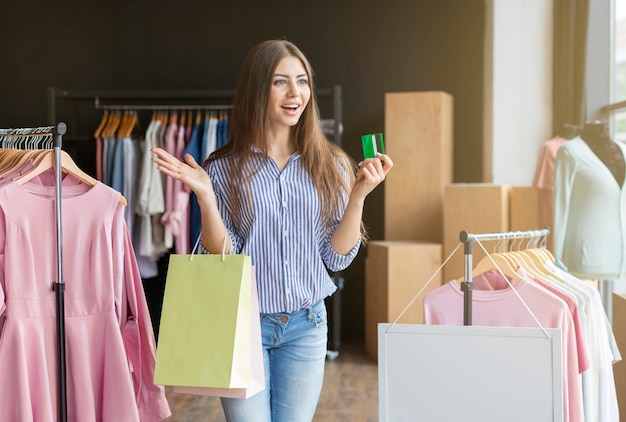 Chica caucásica emocionada mirando hacia otro lado con la boca abierta, sosteniendo bolsas de compras, mostrando tarjeta de crédito, espacio de copia