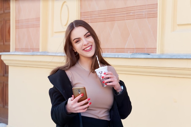 Chica caucásica joven caminando por la calle sosteniendo una taza de café para llevar