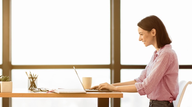 Una chica caucásica sonriente trabajando con una computadora portátil en la oficina