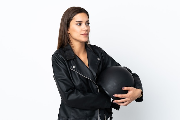 Chica caucásica sosteniendo un casco de motocicleta en la pared blanca mirando hacia el lado