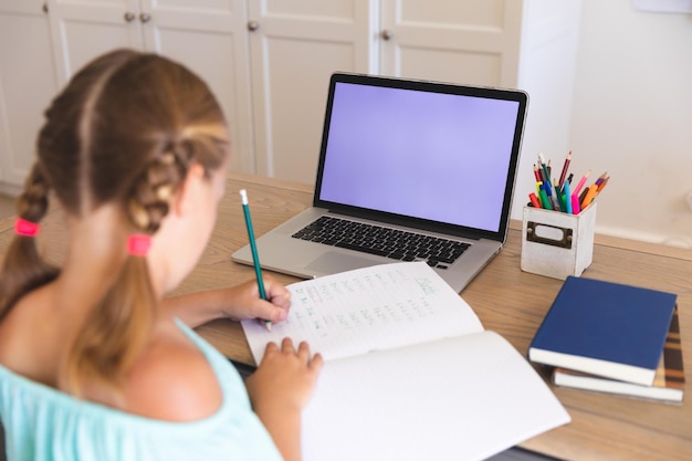 Chica caucásica con videollamada durante la clase en una laptop con espacio para copiar, sentada en el escritorio en casa