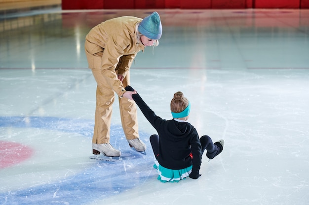 Chica cayendo en patinaje sobre hielo y entrenador ayudándola