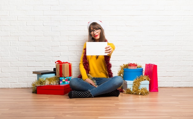 Chica celebrando las fiestas navideñas sosteniendo un cartel blanco vacío para insertar un concepto