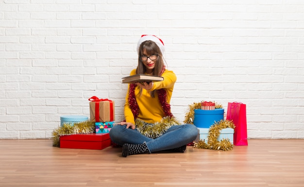 Foto chica celebrando las fiestas navideñas sosteniendo un libro y entregándolo a alguien