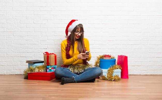 Chica celebrando las vacaciones navideñas enviando un mensaje o correo electrónico con el móvil.