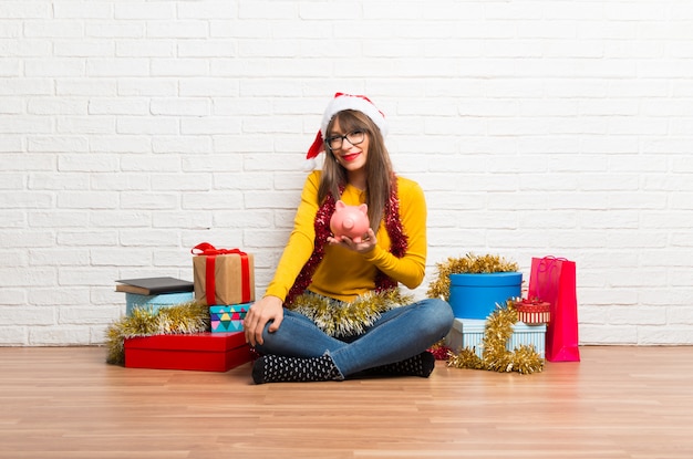 Chica celebrando las vacaciones navideñas tomando una alcancía y feliz porque está llena.