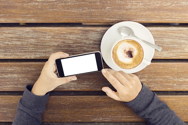 Chica con un celular en blanco y una taza de café en una mesa de madera