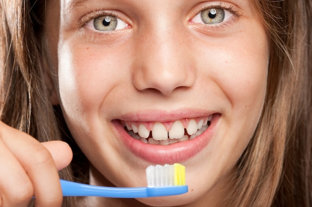 Chica cepillando sus dientes sobre un fondo gris