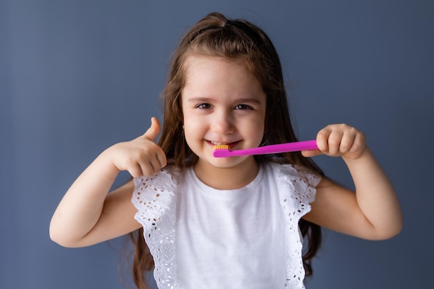 Una chica con un cepillo de dientes rosa y un pulgar hacia arriba