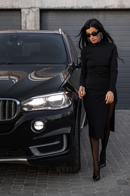 Una chica cerca del auto con un vestido negro.