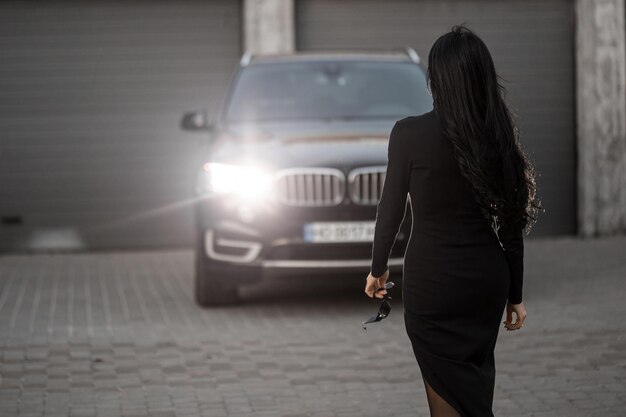 Una chica cerca del auto con un vestido negro.