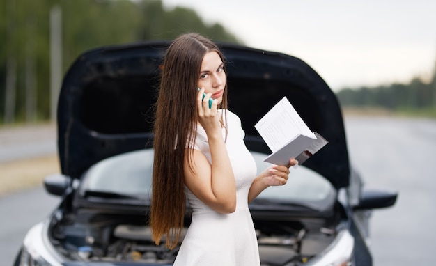 Chica cerca de coche roto en la carretera está llamando al teléfono móvil.