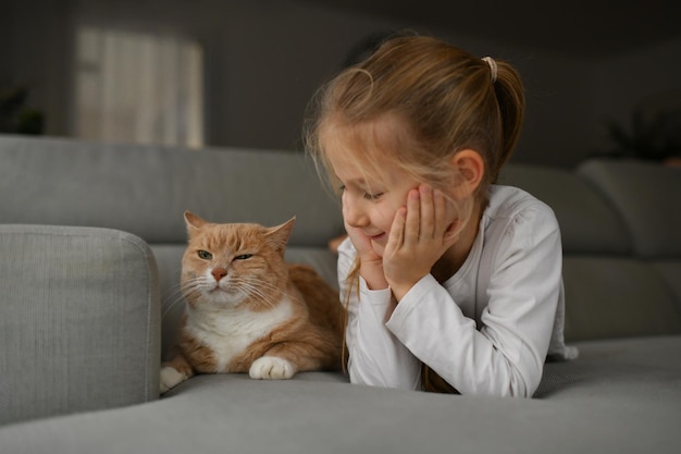 Una chica cerca de un gato pelirrojo en el sofá.