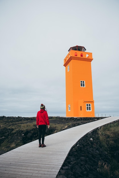 Chica cerca del gran faro naranja en Islandia. Panorama artístico del concepto de moda y naturaleza.