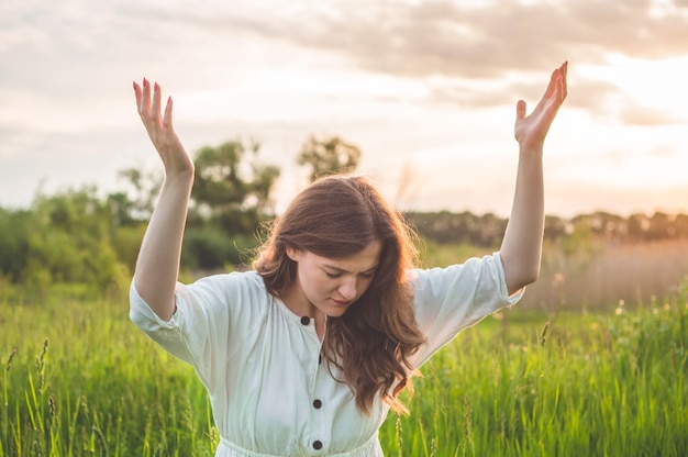 Chica cerró los ojos, rezando en un campo durante la hermosa puesta de sol