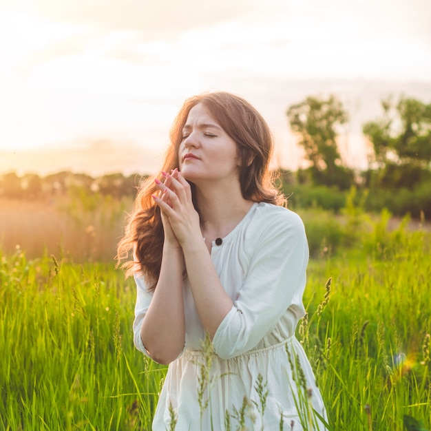 Chica cerró los ojos, rezando en un campo durante la hermosa puesta de sol