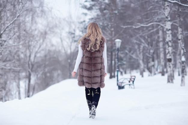 chica en un chaleco de piel camina en el exterior de invierno / modelo joven adulto en piel de ropa de invierno