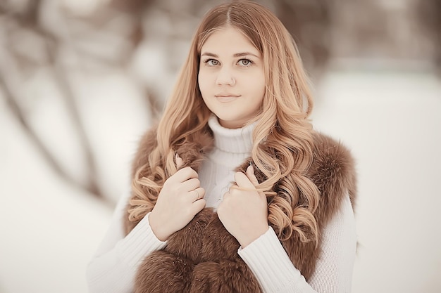 chica en un chaleco de piel camina en el exterior de invierno / modelo joven adulto en piel de ropa de invierno