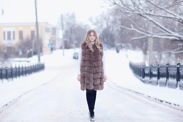 chica en un chaleco de piel camina en el exterior de invierno / modelo joven adulto en piel de ropa de invierno