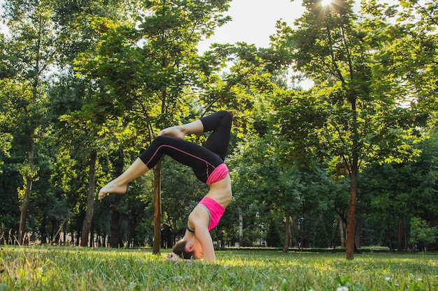 chica en un chándal ligero haciendo yoga en el parque por la tarde en el verano