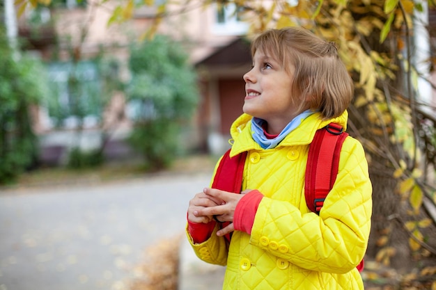 Chica con chaqueta amarilla y maletín rojo en la calle en otoño