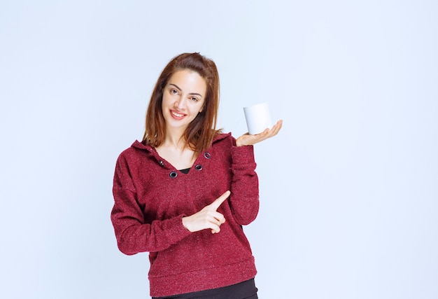 Chica de chaqueta roja sosteniendo una taza de café con leche.