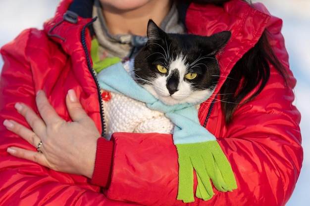 Una chica con una chaqueta roja sostiene un gato blanco y negro en sus brazos.