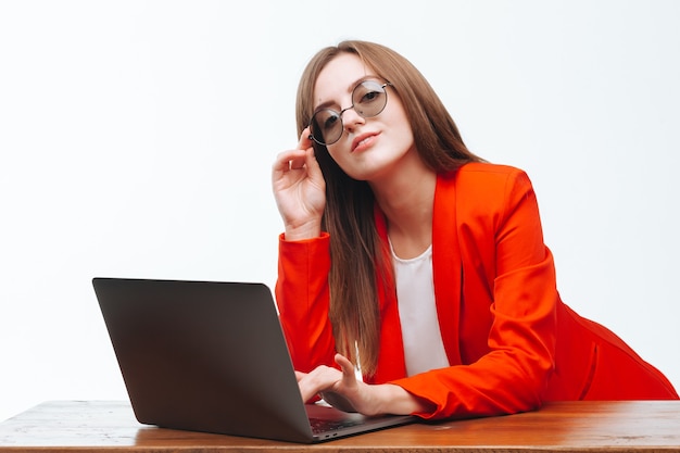 Chica en una chaqueta roja trabajando en la computadora sobre un fondo blanco.