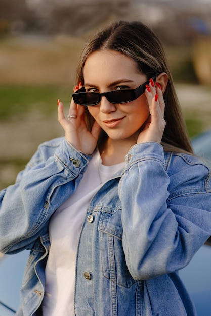 Una chica con chaqueta vaquera y gafas de sol mira a la cámara.