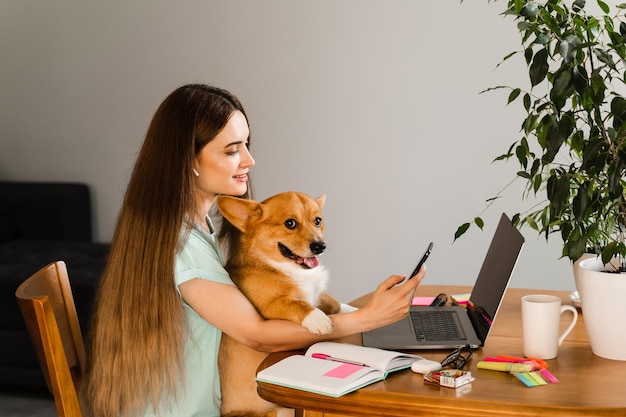 Chica chateando con amigos en línea usando una computadora portátil y mostrando su perro Corgi en casa Estilo de vida con Welsh Corgi Pembroke Conexión de video con la familia Chica feliz y mascota doméstica divirtiéndose juntos