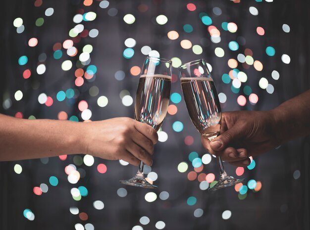 Una chica y un chico se aparean con copas de champán en un hermoso bokeh festivo de luces