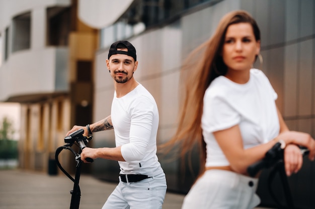 Una chica y un chico caminan en patinetes eléctricos por la ciudad, una pareja enamorada en patinetes.