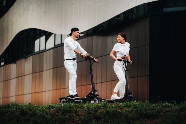 Una chica y un chico caminan en patinetes eléctricos por la ciudad, una pareja enamorada en patinetes.