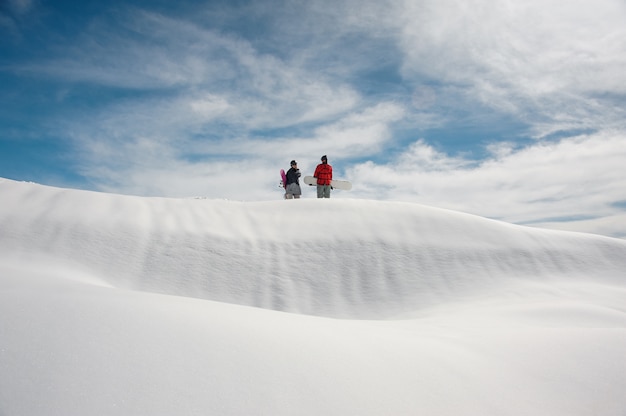 Chica y chico en equipo de esquí con tablas de snowboard en manos están parados en carretera cubierta de nieve