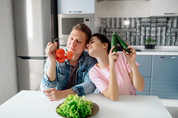 Una chica y un chico están sentados en la cocina eligiendo verduras para una deliciosa cena vegana.