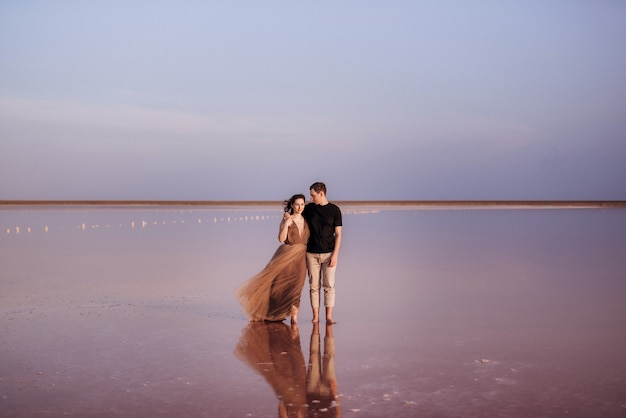 Chica y chico en la orilla de un lago salado rosa al atardecer