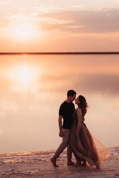 Chica y chico en la orilla de un lago salado rosa al atardecer