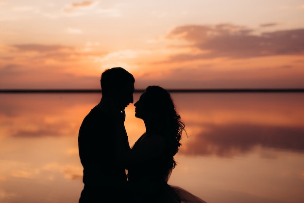 Chica y chico en la orilla de un lago salado rosa al atardecer