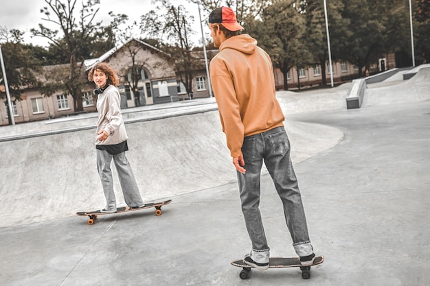 Chica y chico en patinetas deslizándose en skatepark