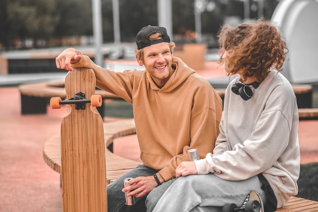 Chica y chico con patinetas hablando sentado en un banco