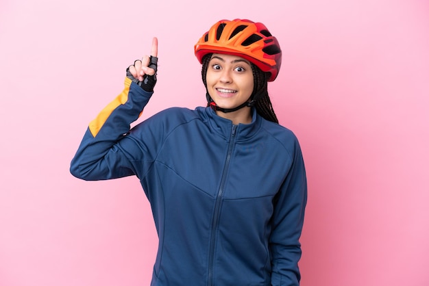 Chica ciclista adolescente aislada de fondo rosa señalando una gran idea