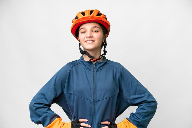 Chica ciclista adolescente sobre fondo blanco aislado posando con los brazos en la cadera y sonriendo